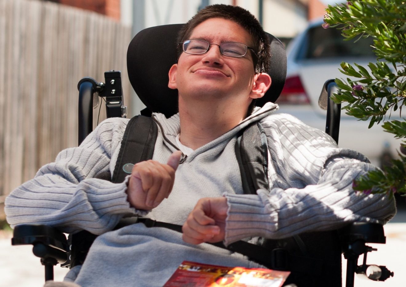 A young male wheelchair user out the front of his house in the driveway after collectuing the mail.