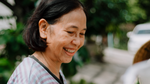 Older woman smiling outside in a garden.