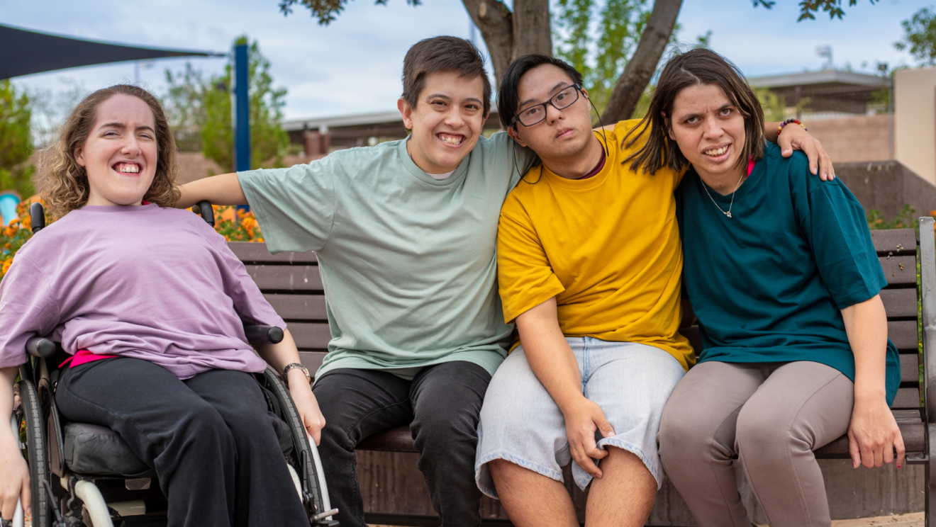 Social model 2 - People with Disability Australia Four young people with disability smiling in a park with their arms around each other.